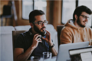 Man holding headphones around his neck looking at laptop